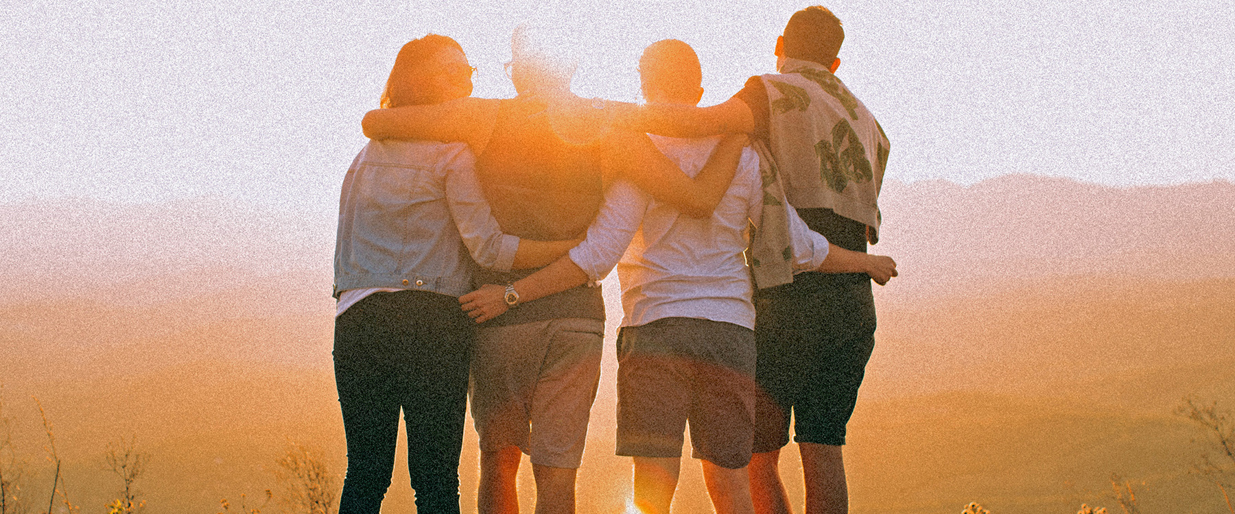 4 people hugging in front of a sunset