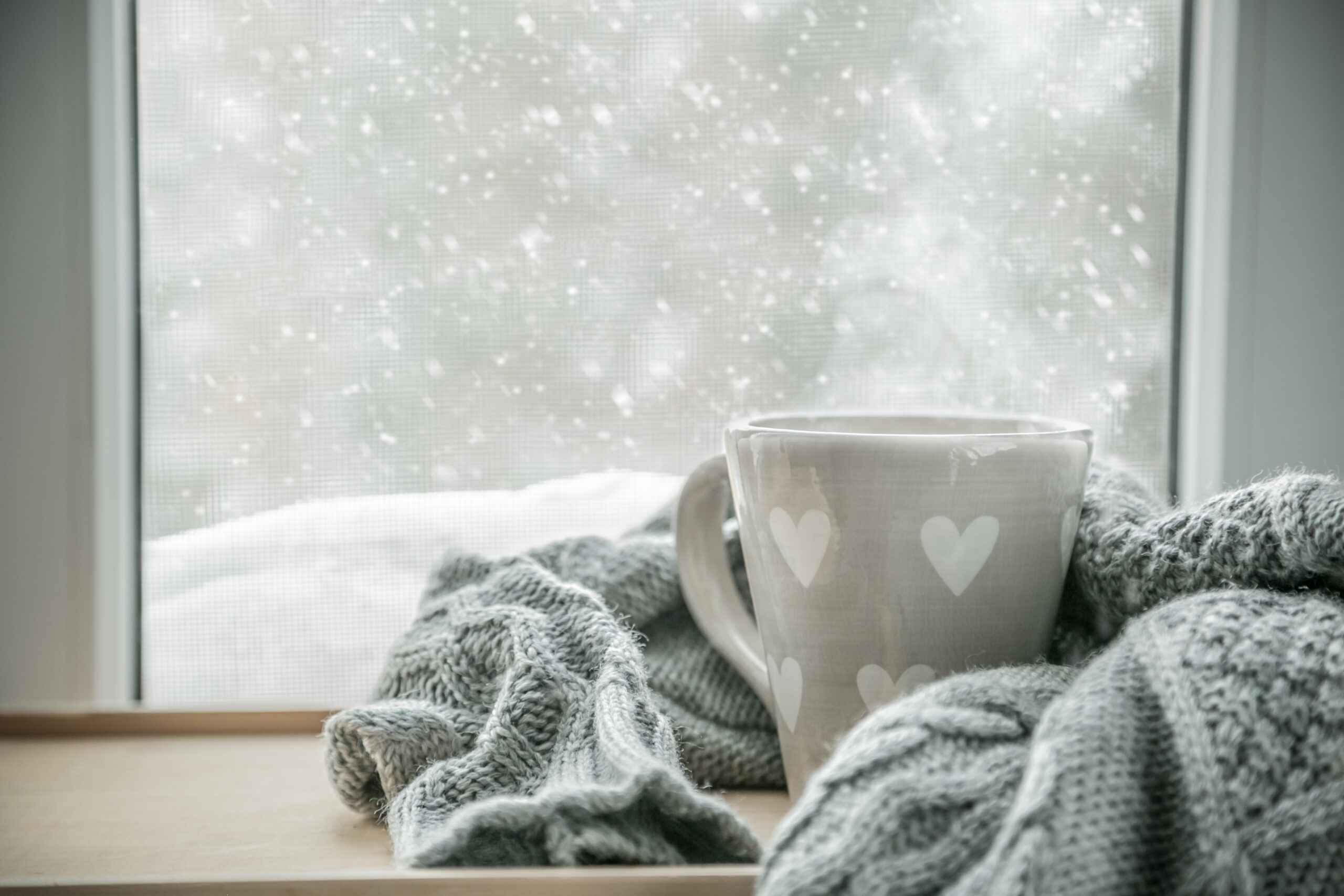 Gray mug wrapped in blanket with snow falling outside