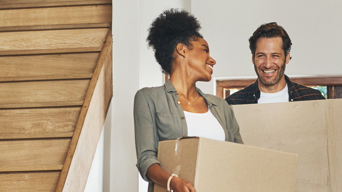 Couple smiling while carrying moving boxes