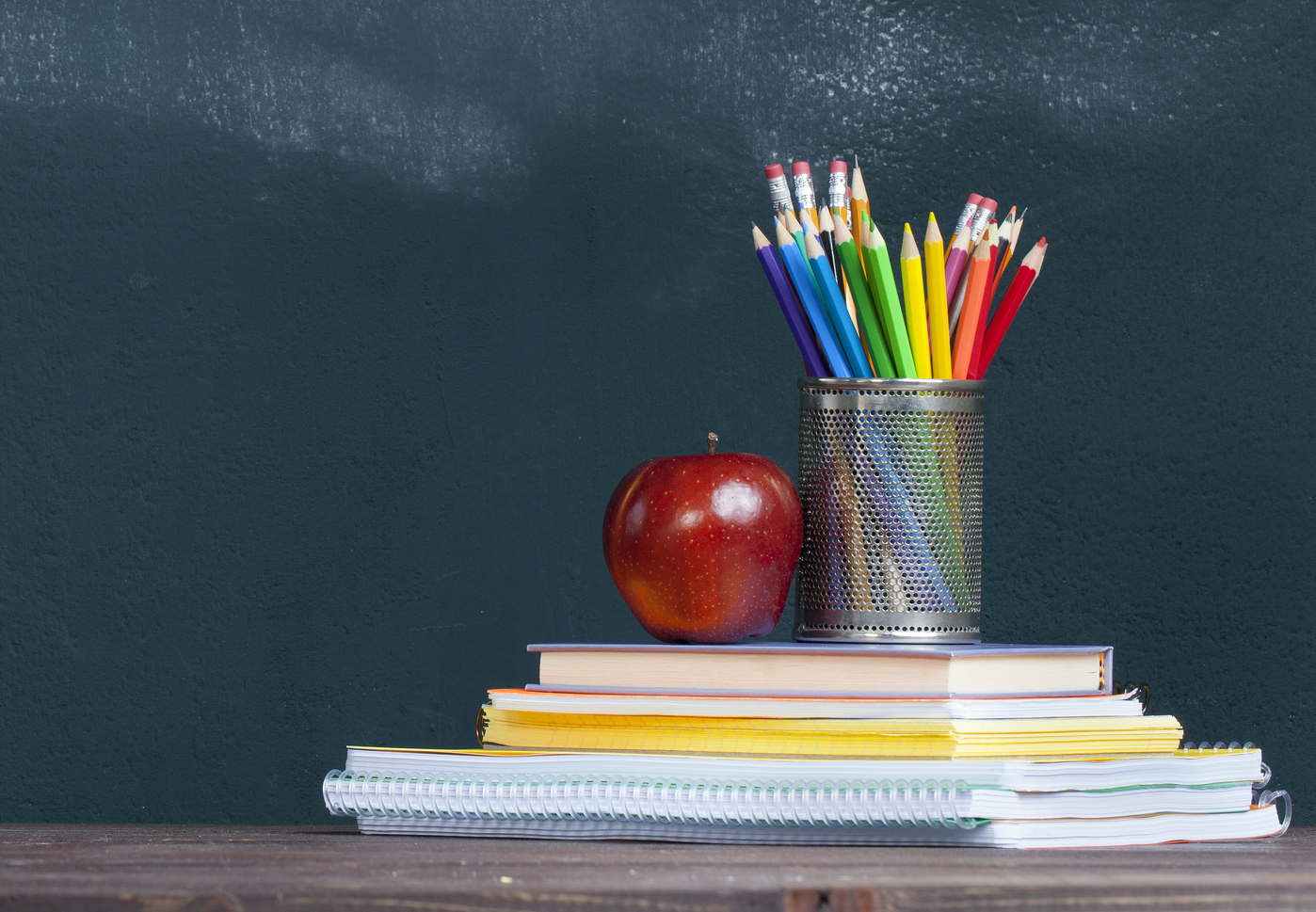 Schoolbooks, pencils, and apple sit in front of a blackboard