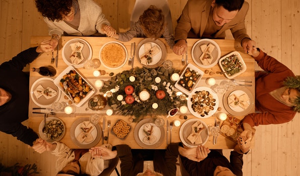 Holiday dinner with dinner guests holding hands around a table of food.
