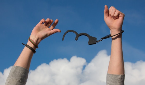 Arms breaking out of handcuffs with a blue sky behind them.
