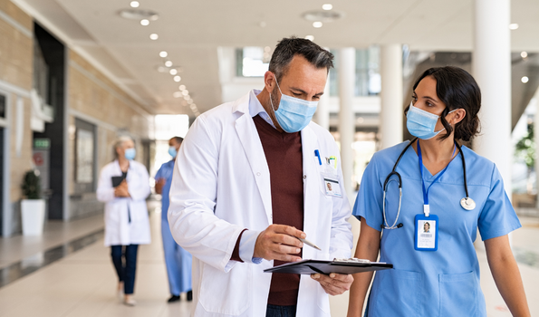 A physician and health professional walk together down a hallway reviewing a chart. 