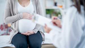 A pregnant person touches their stomach as they talk to a doctor.