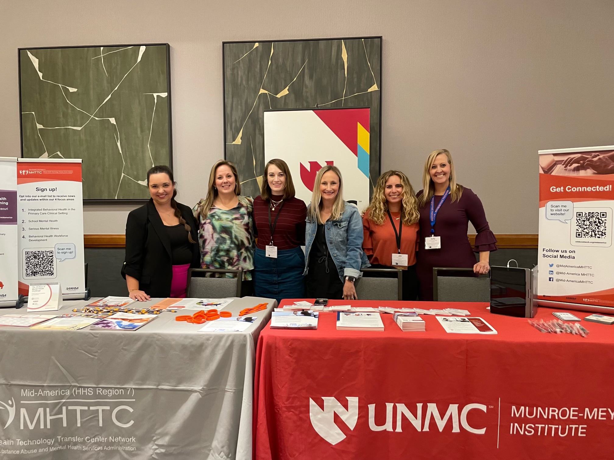 Members of the Mid-America MHTTC pose behind a booth at a conference. 