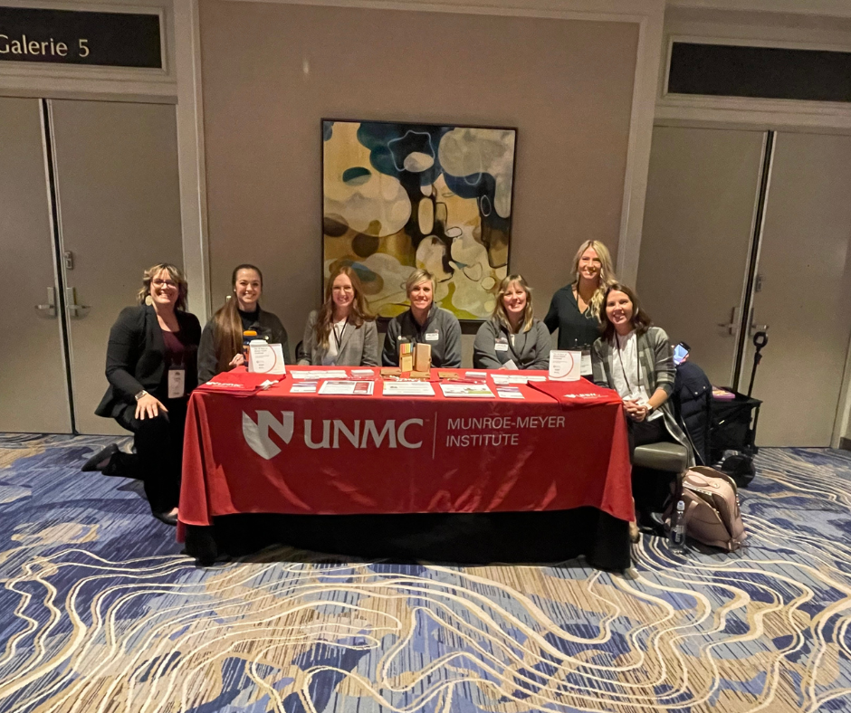 A group of women sit behind a table that says "UNMC Munroe-Meyer Institute"