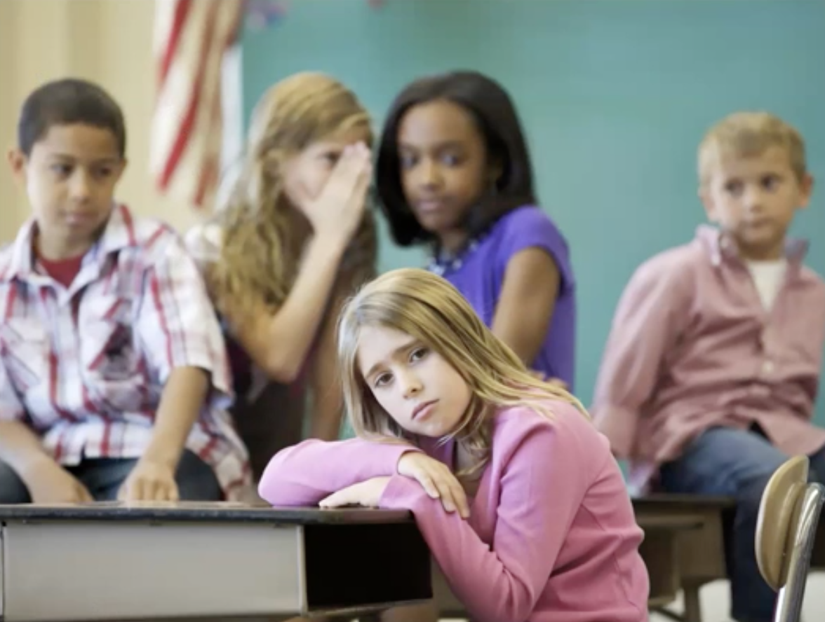 Young student looks troubled near a group of teasing classmates
