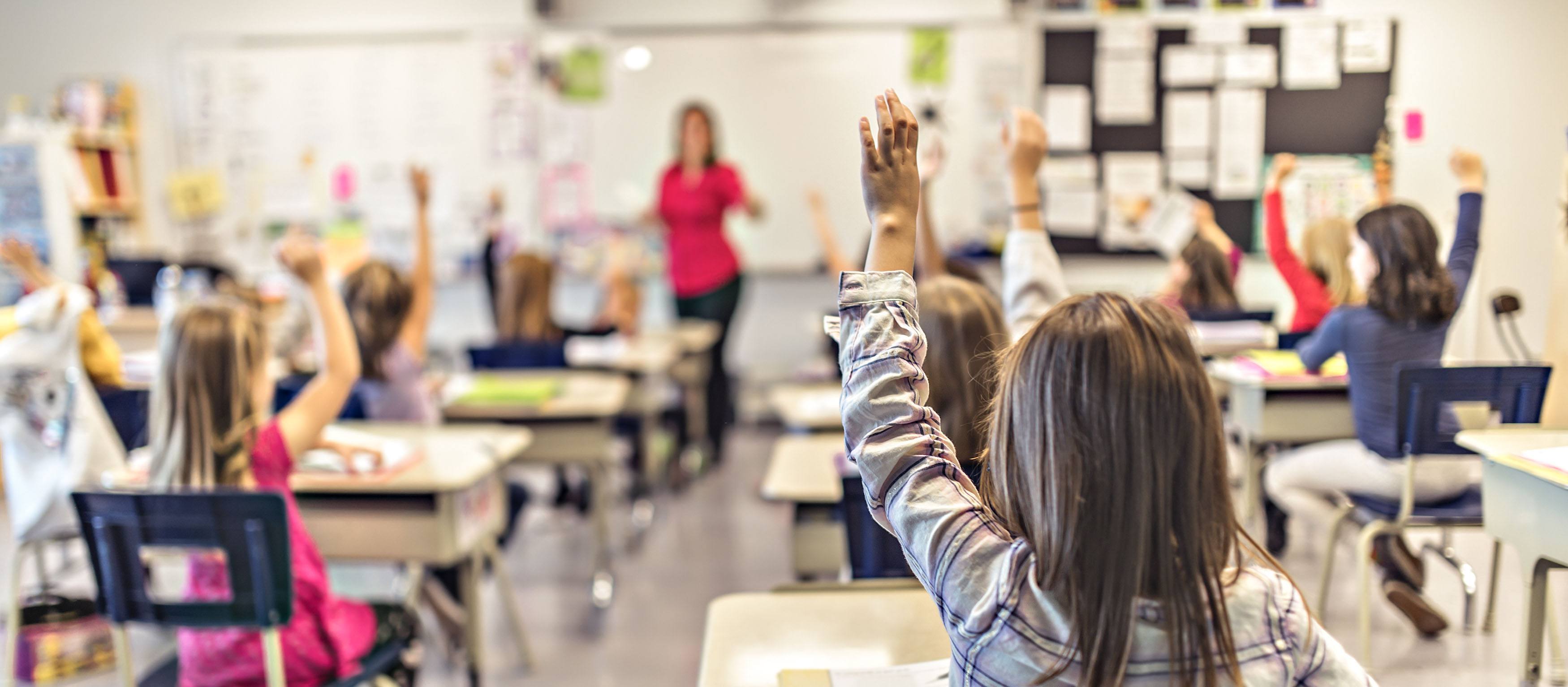 Elementary children at desks raising their hands in classroom